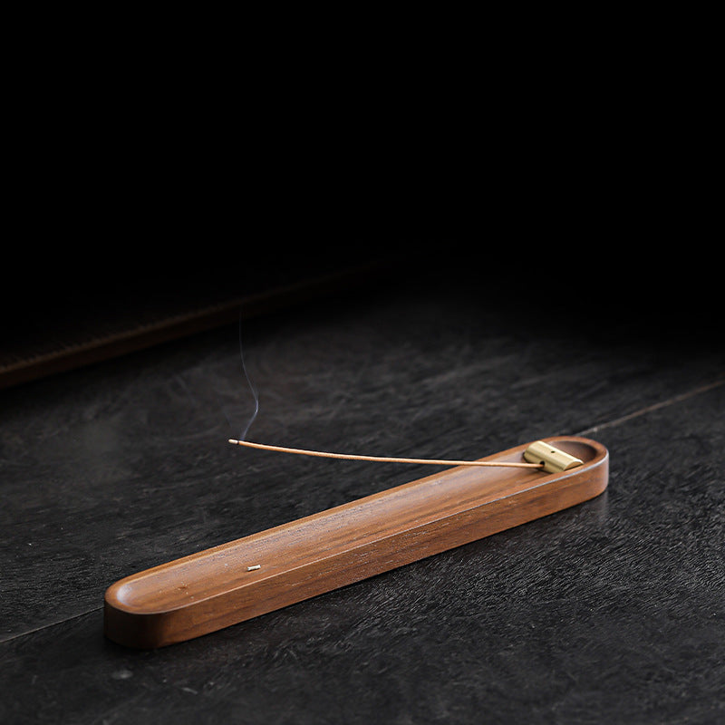 Walnut and brass incense holder on a dark tabletop