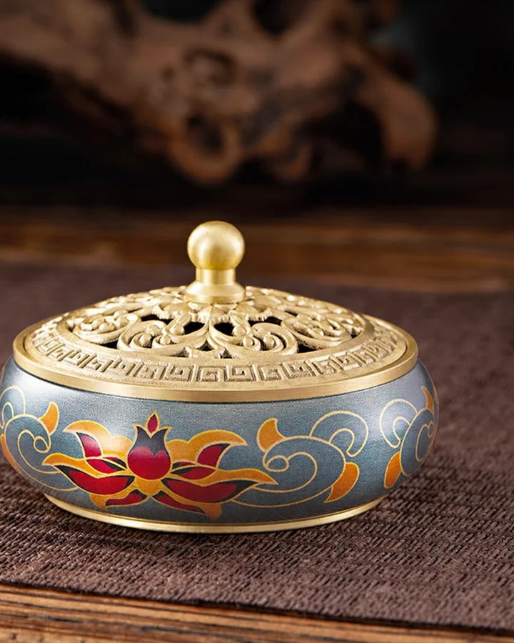 A painted lotus brass incense burner on a dark woven mat